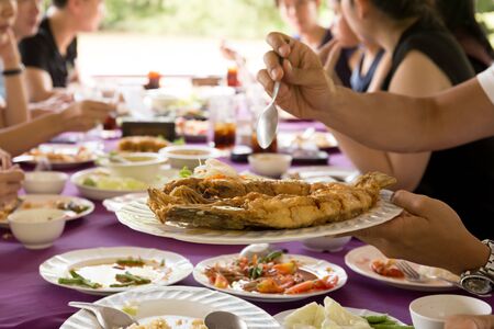Group of friend enjoying  lunch with hand holding deep fried fish in Thai style food and drinkの写真素材