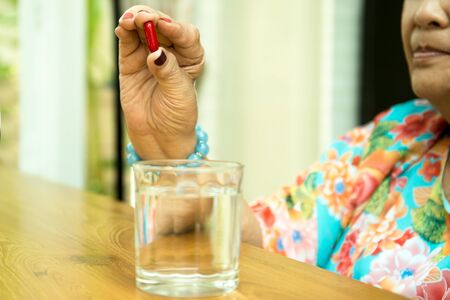 Health care concept senior woman hand holding pills with and glass of water on wooden tableの写真素材