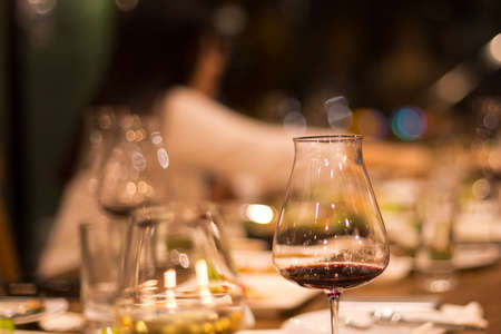 Candid shot in high iso with low light selected focus glass of red wine with people having dinner in restaurantの写真素材