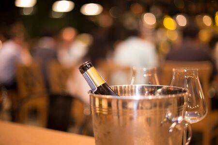 Bottle of wine in ice bucket with wine glasses with bokeh light in backgroundの写真素材