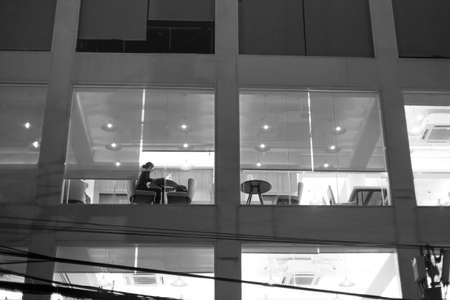 Unidentified woman working late night in coffee shop shot through  glass window black and whiteの写真素材