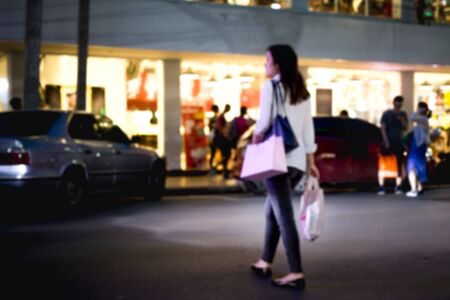Blurred concept woman crossing the road with shopping bag at nightの写真素材