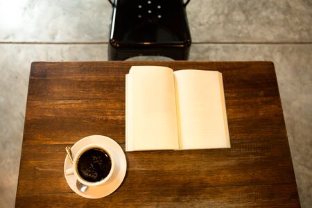 Top view cup of coffee on wooden table with open book and black metal chairの写真素材