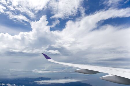 Plane wing flying over white clouds and oceanの写真素材