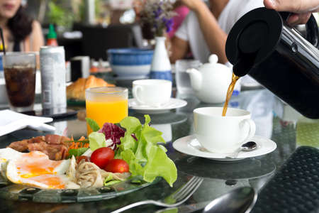 Waiter pouring coffee with breskfat set on table having fried eggs and vegetable salad with tea pot ready for eat with friendの写真素材