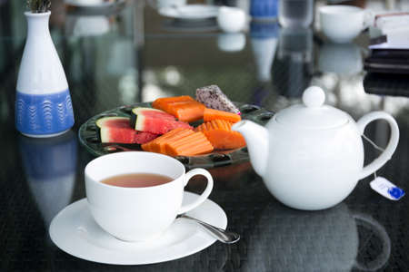 Cup of tea and tea pot with fresh fruit salad on glass tableの写真素材