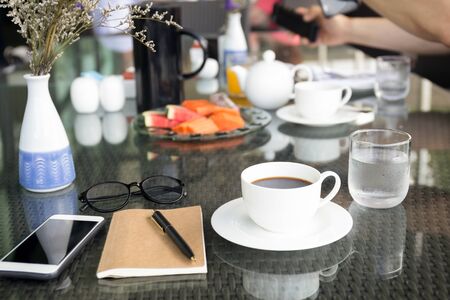 Cup of coffee and notebook with glasses pen with cell phone on glass tableの写真素材