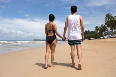 Couple holding hands walking on beach on vacation in Thailandの写真素材