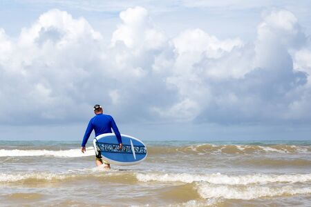 Surfer walking into the sea wave with surf boardの写真素材