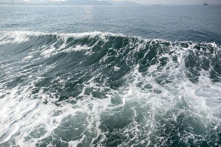 Deep blue ocean wave foam with fishing boat in backgroundの写真素材
