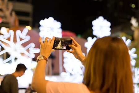 Woman hand holding mobile phone take a photo of christmas tree  and lightの写真素材