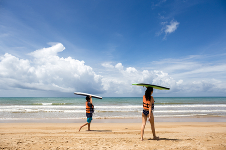 Young boy and girl with surfing boards walking on tropical ocean beachの写真素材