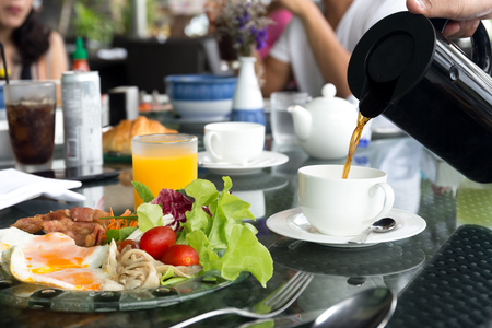 Waiter pouring coffee with breskfat set on table having fried eggs and vegetable salad with tea pot ready for eat with friendの写真素材