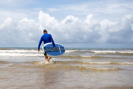 Surfer walking into the sea wave with surf boardの写真素材