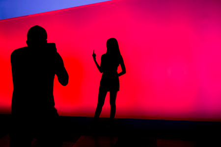 Silhouettes of people taking photo on colourful led screen in backgroundの写真素材