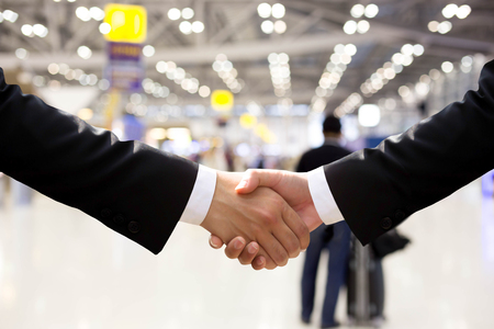Business hand shake in airport building with bokeh light in backgroundの写真素材