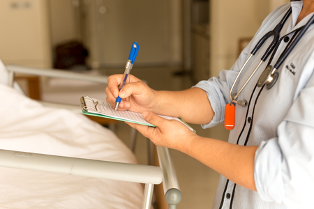 Woman doctor writing medical details of patient in hospitalの写真素材