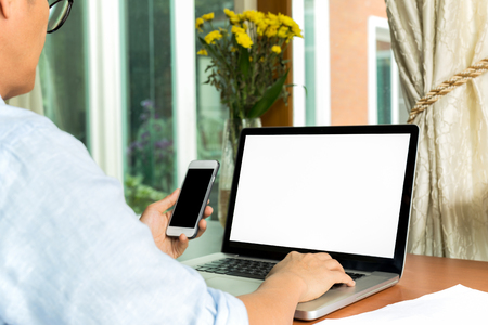Business man hand holding cell phones and working on laptop on tableの写真素材