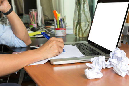 Man writing on paper work and laptop with crumpled papers ball on desk of misteakn