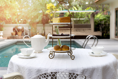 Afternoon tea with cup of tea and teapot on table with cake by swimming poolの写真素材