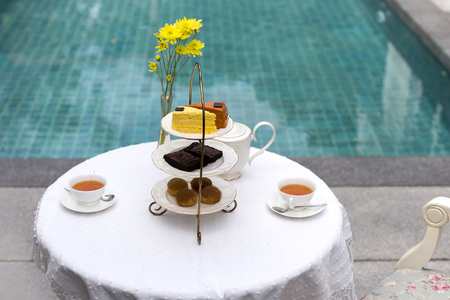 Afternoon tea with cup of tea and teapot on table with cake by swimming poolの写真素材