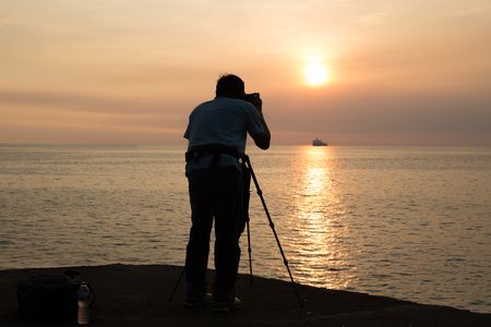 Silhouette photographer taking photo of ocean at and sunset with fishing boatの写真素材
