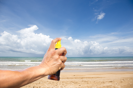 conceptual hand spraying sunscreen protection oil with beach and blue skyの写真素材