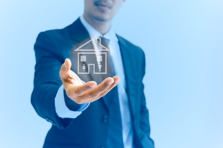 Conceptual businessman hand holding a house with woman and men icon in blue backgroundの写真素材