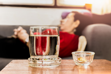 Selected focus on pills with glass of water on table with senior women sleeping on couchの写真素材