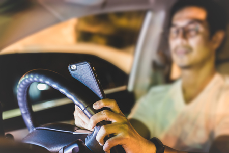 Dangerous concept man using cell phone while driving at nightの写真素材