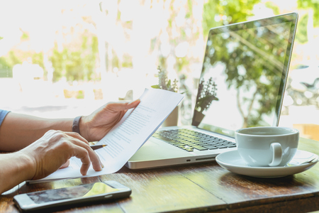 Businessman hand holding pen over agreement form with laptop and coffee on tableの写真素材