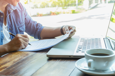 Businessman hand holding pen over agreement form with laptop and coffee on tableの写真素材