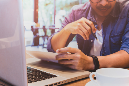Businessman hand holding pen over agreement form with laptop and coffee on tableの写真素材