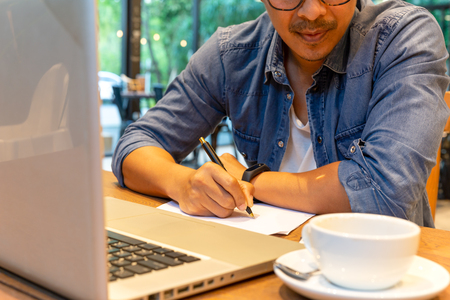Man hand holding pen over agreement form with laptop and coffee on tableの写真素材