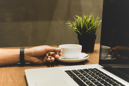 Slected focus hand holding coffee cup with lapyop on wooden table in matte colorの写真素材