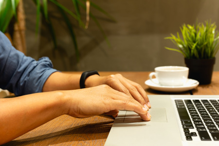 Man hands working on keyboard laptop with coffee cup on wooden tableの写真素材