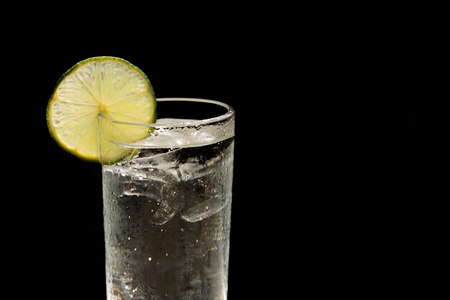 Glass of fresh drinking water with slice of lime isolated in black backgroundの写真素材