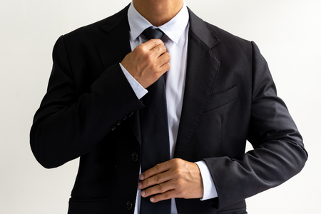 Businessman in black suit tying the necktie in white backgroundの写真素材