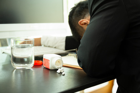 Pills spilling out of pill bottle with businessman fall asleep on the desk overworked.の写真素材