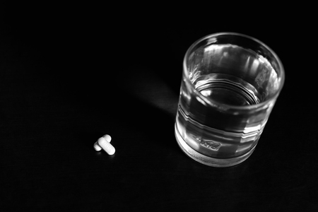 Conceptual glass of water and pills on wooden table in black and white in blue filterの写真素材