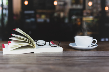 Selected focus of coffee cup with open book and glasses on wooden table in matte colorの写真素材
