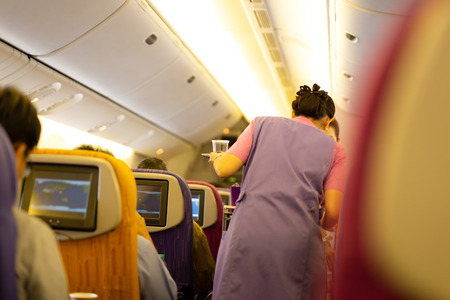 Interior of airplane with passengers on board with flight attendant serving food and beverage