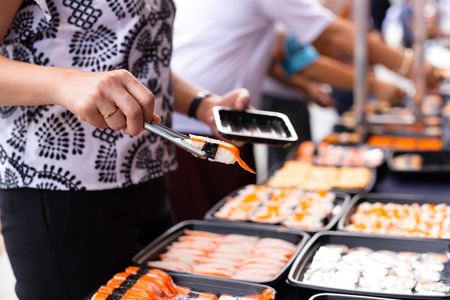 Hand picking sushi roll from food stall at event street market in Thailandの写真素材