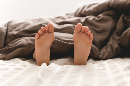 Young boy bare feet in bed under blanket.の写真素材