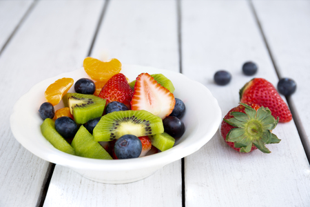 Fresh fruit salad in a white plate on white wooden tableの写真素材