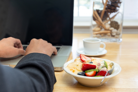 Businessman working on laptop and having bowl of yogurt with fruit salad and coffeeの写真素材