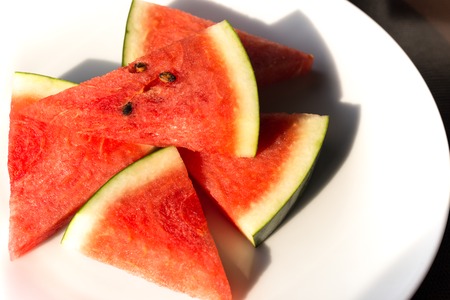 Slices of watermelon on a white plate with sunlignt in the morningの写真素材