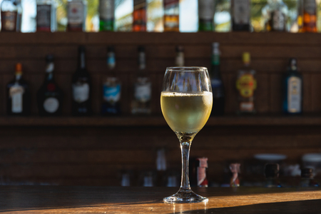 Glass of white wine on top of wooden counter bar with sunlight.の写真素材