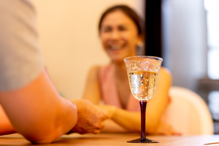Glass of white wine on the table with couple holding hands on a date.の写真素材