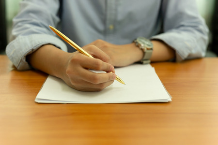 Female hand with pen on document form on wooden table.の写真素材